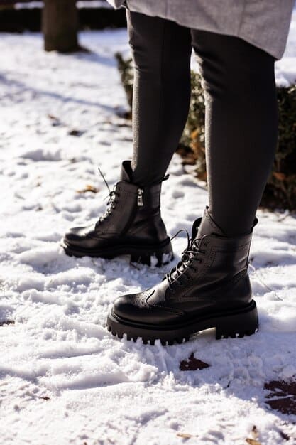 A pair of chunky, lug-soled boots standing on a snow-covered ground. The boots are stylishly laced and made of waterproof leather, showcasing their durability and fashionable design.