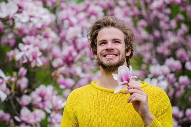 A man standing in a blooming garden, wearing a light jacket and holding a bottle of spring-inspired fragrance. The scene captures the essence of renewal and floral scents.