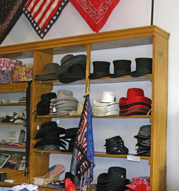 A variety of men's hats displayed on shelves in a boutique, including fedoras, flat caps, and baseball caps. The focus is on textures and colors of the different materials.