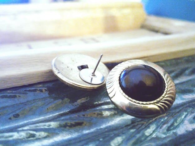 A detailed shot of a variety of cufflinks displayed in a vintage jewelry box. The cufflinks range from classic gold and silver designs to more modern styles with colorful gemstones and unique shapes.