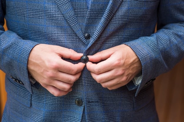 A close-up image of a man's hand adjusting his cufflink while wearing a sharp suit. The cufflink is a sleek, modern design with a matte finish, contrasting with the smooth fabric of the suit. The background is blurred, focusing attention on the hand and cufflink.
