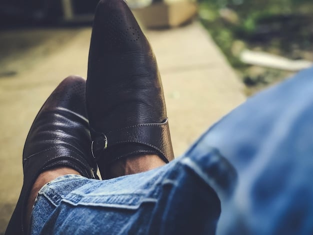 A close-up shot of a man sitting casually, wearing rolled-up denim jeans and a pair of socks with a geometric pattern in shades of blue and gray. The socks complement his light-colored sneakers, and the focus is on the intricate design and texture of the socks, highlighting their role as a stylish accessory.