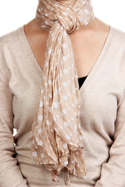A woman's hands adjusting a patterned silk scarf around her neck. The scarf features a mix of geometric patterns in shades of blue, orange, and white. She also wears a plain white blouse which helps to highlight colors. The background is blurred to focus attention is on the scarf and the persons hands.