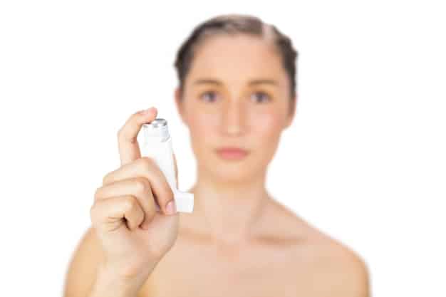 A person is holding an eau de toilette bottle and spraying it into the air against a light background, capturing the mist and the transparent bottle.