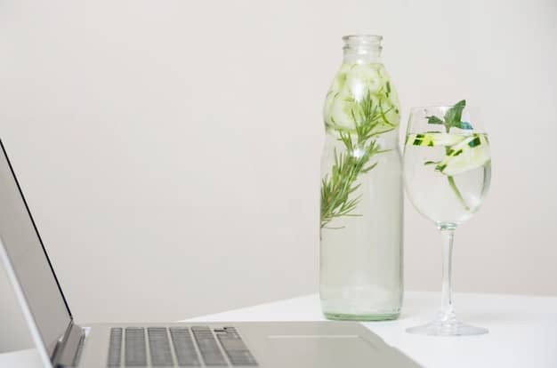 A minimalist workspace with a clean desk, a laptop, a small vase with rosemary sprigs, and an essential oil diffuser emitting a gentle mist.